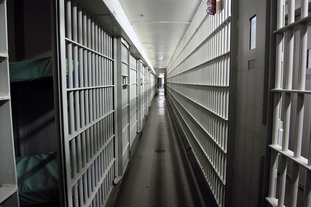 A black and white image of a prison hallway of cells, with bars